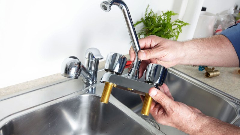 a close-up of plumbing service contractor’s hands installing a kitchen sink faucet