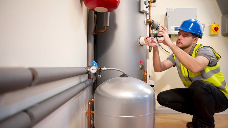 A technician in working clothes and a hard hat is delivering water heater repair services.
