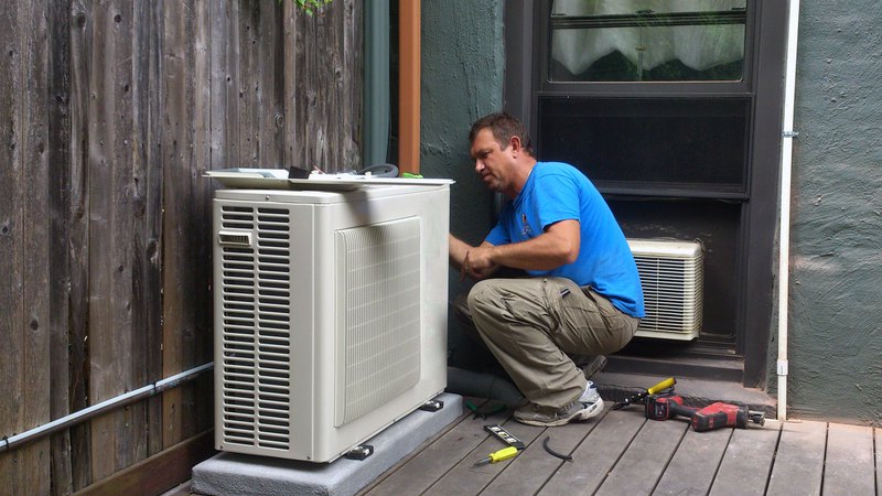 A technician is performing ductless heat pump installation: a unit is mounted in the patio corner.